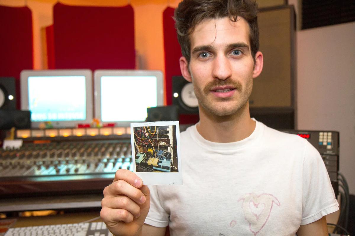 Jeremy Mendicino at a recording console, holding a Polaroid of studio gear